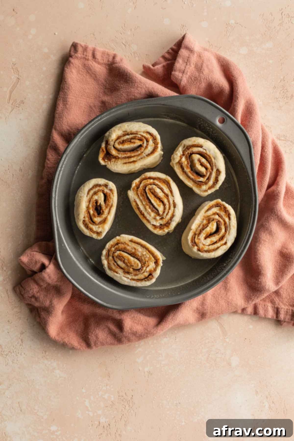 Pre-baked cinnamon rolls arranged snugly in a round cake pan, ready for the air fryer.