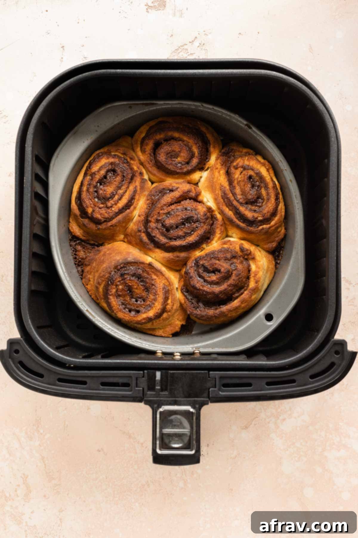 Overhead view of perfectly baked, golden-brown cinnamon rolls inside the air fryer basket.