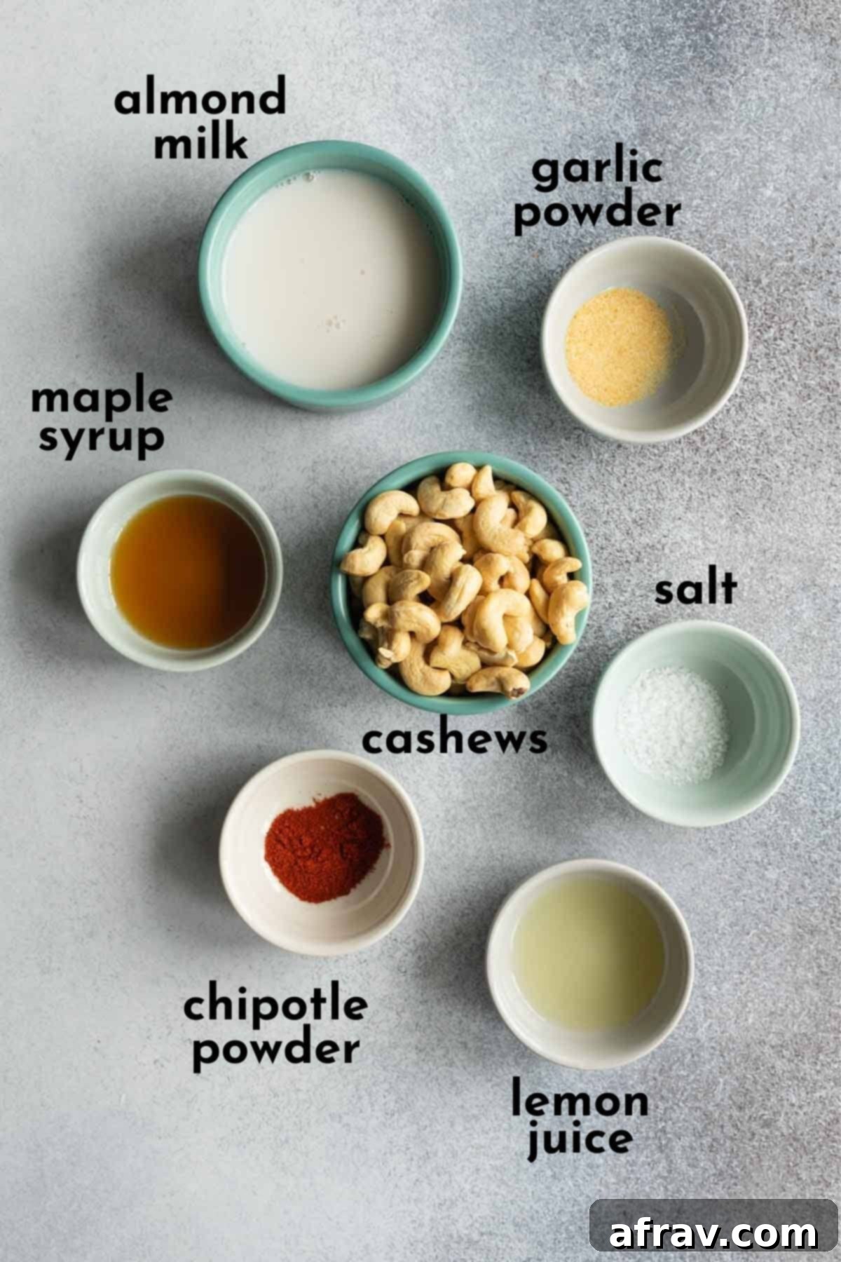 Individually arranged ingredients for making vegan chipotle dip: cashews, non-dairy milk, lemon juice, maple syrup, chipotle powder, garlic powder, and salt.