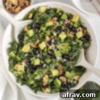 A vibrant superfood salad, featuring fresh blueberries, crisp broccoli, crunchy walnuts, and creamy avocado, presented in a pristine white serving bowl with elegant white salad utensils, inviting a healthy and delicious meal.