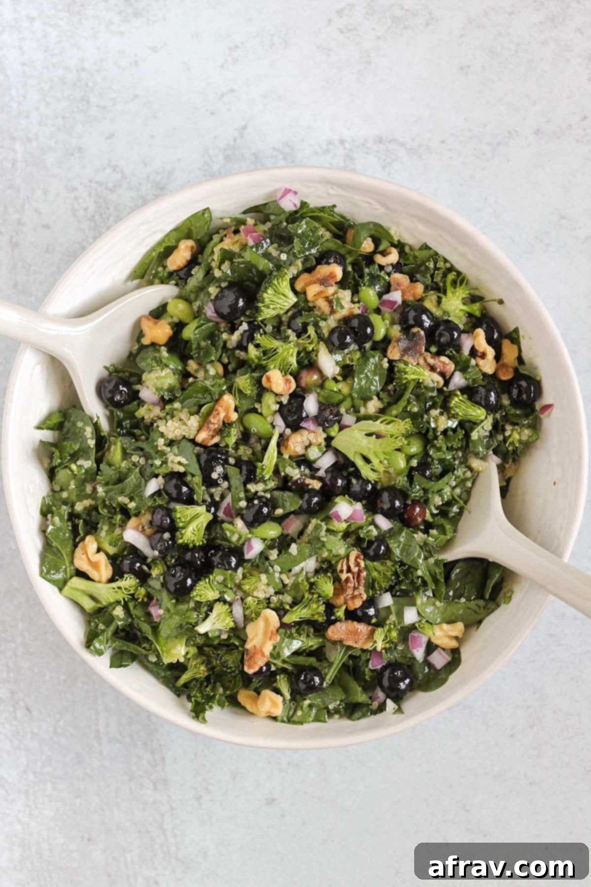White salad utensils actively mixing up the colorful superfood salad ingredients in a spacious white bowl, ensuring all components are evenly coated with dressing.