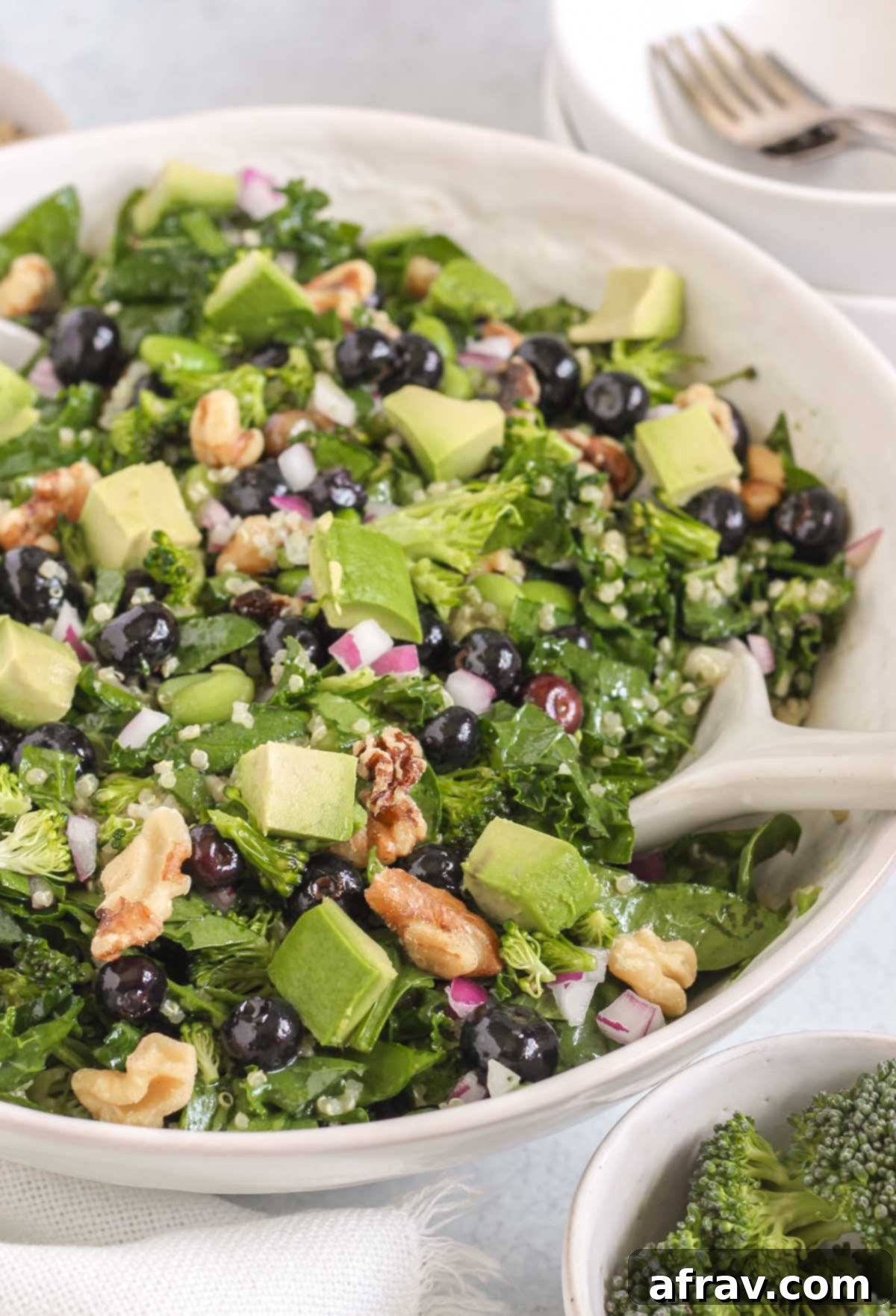 A beautifully presented superfood salad in a large white bowl, garnished with freshly chopped avocado. Two small individual salad bowls and forks are visible in the background, set for serving.