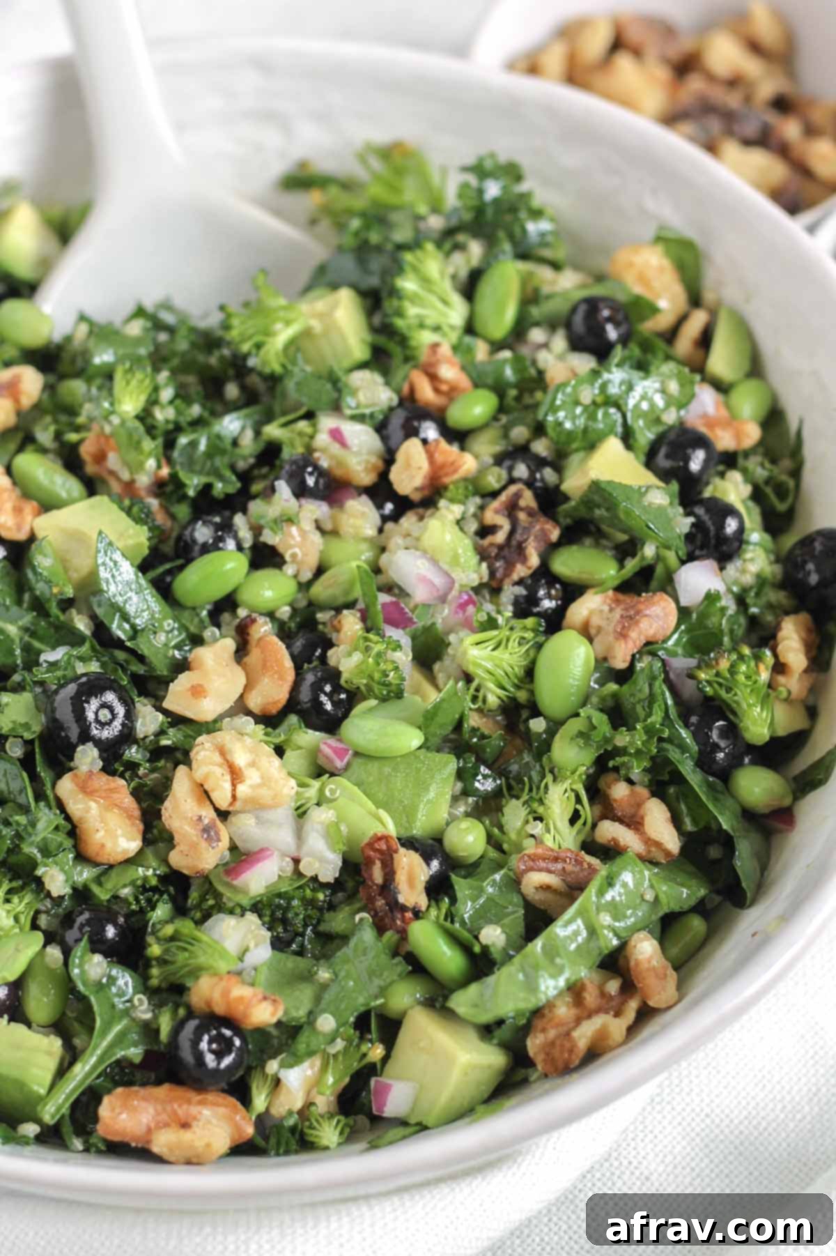Power-Packed Superfood Salad 10 A large white bowl filled with Superfood Salad, featuring a white serving utensil ready to serve. In the background, a small bowl of walnuts adds a rustic touch, highlighting the wholesome ingredients.