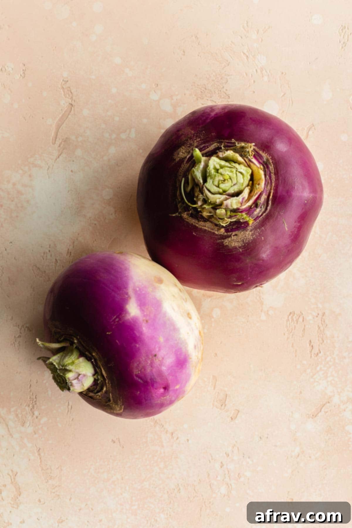 Two unpeeled turnips on a pink surface.