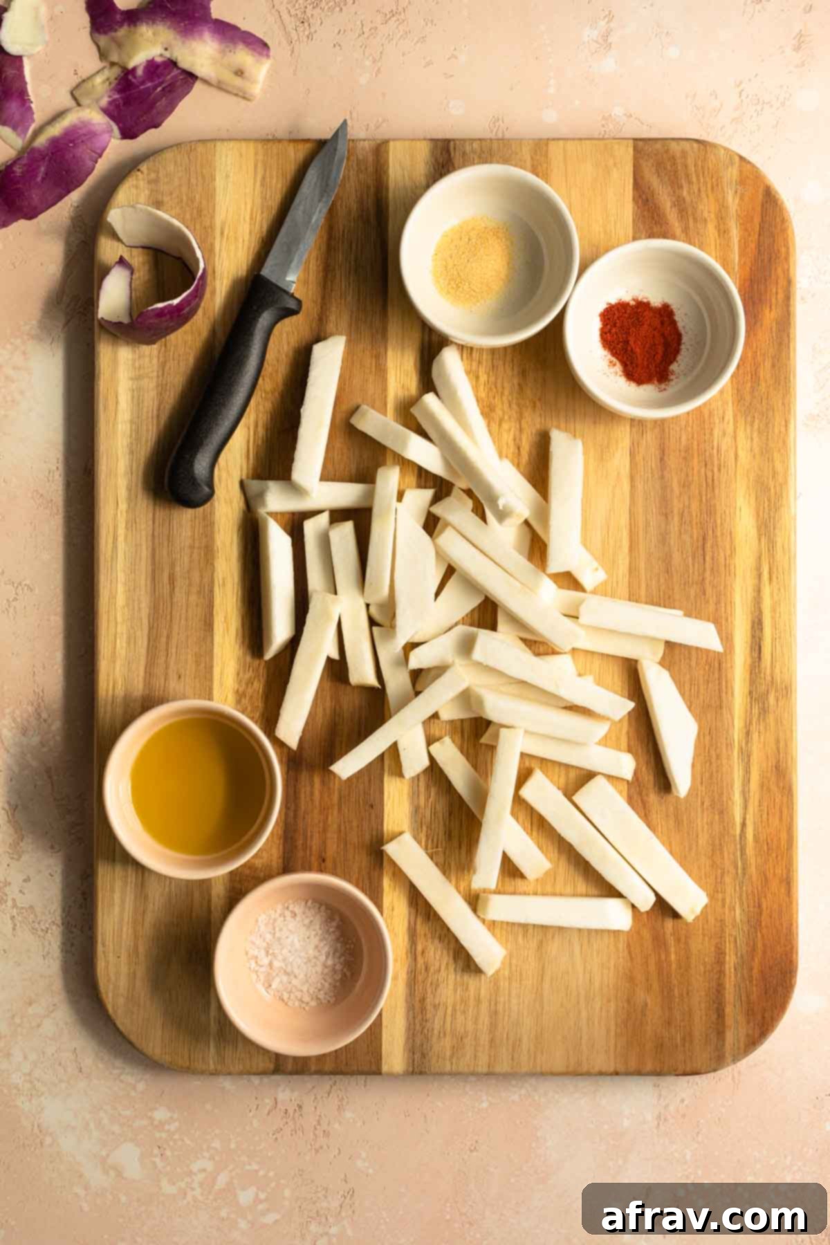 Raw turnip fries on a wooden cutting board with dishes of oil and seasonings on the side.