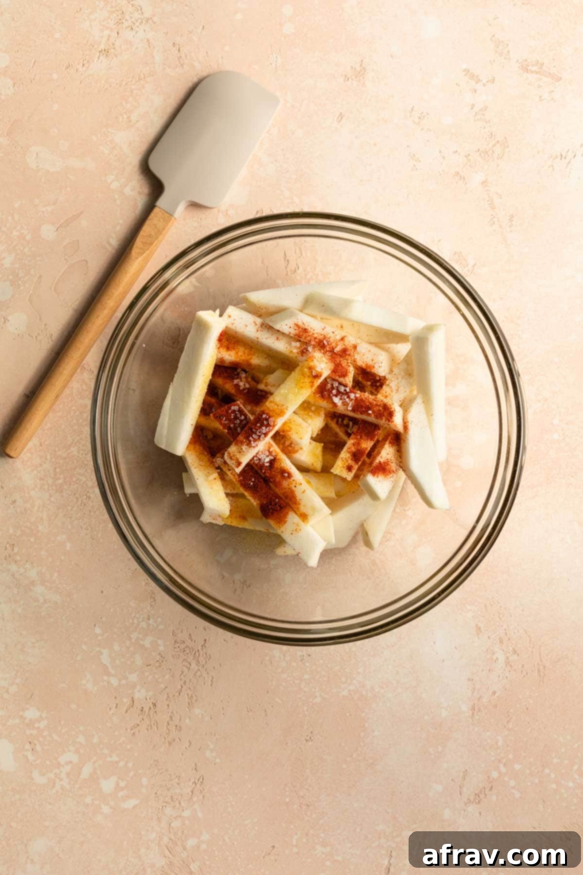 Raw turnip fries in a glass bowl with oil and seasonings on top.