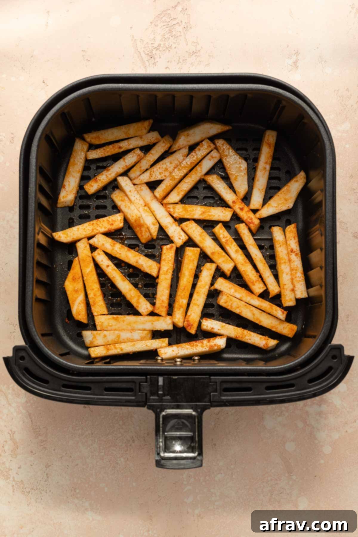 Seasoned raw turnip fries arranged in a single layer in an air fryer basket.