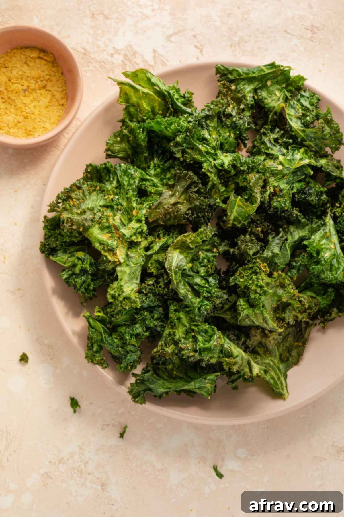 Overhead view of kale chips on a pink plate, showcasing their perfect crispiness and golden-green color, ready to be enjoyed as a healthy snack or side.