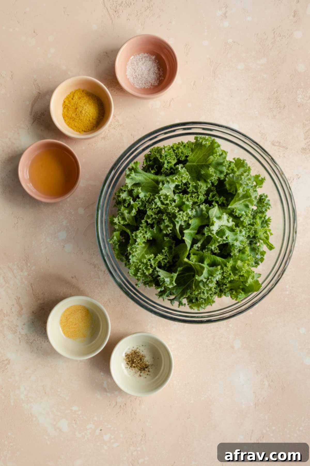 A vibrant selection of fresh ingredients, including curly kale, avocado oil, nutritional yeast, garlic powder, salt, and pepper, meticulously arranged before making air fryer kale chips.