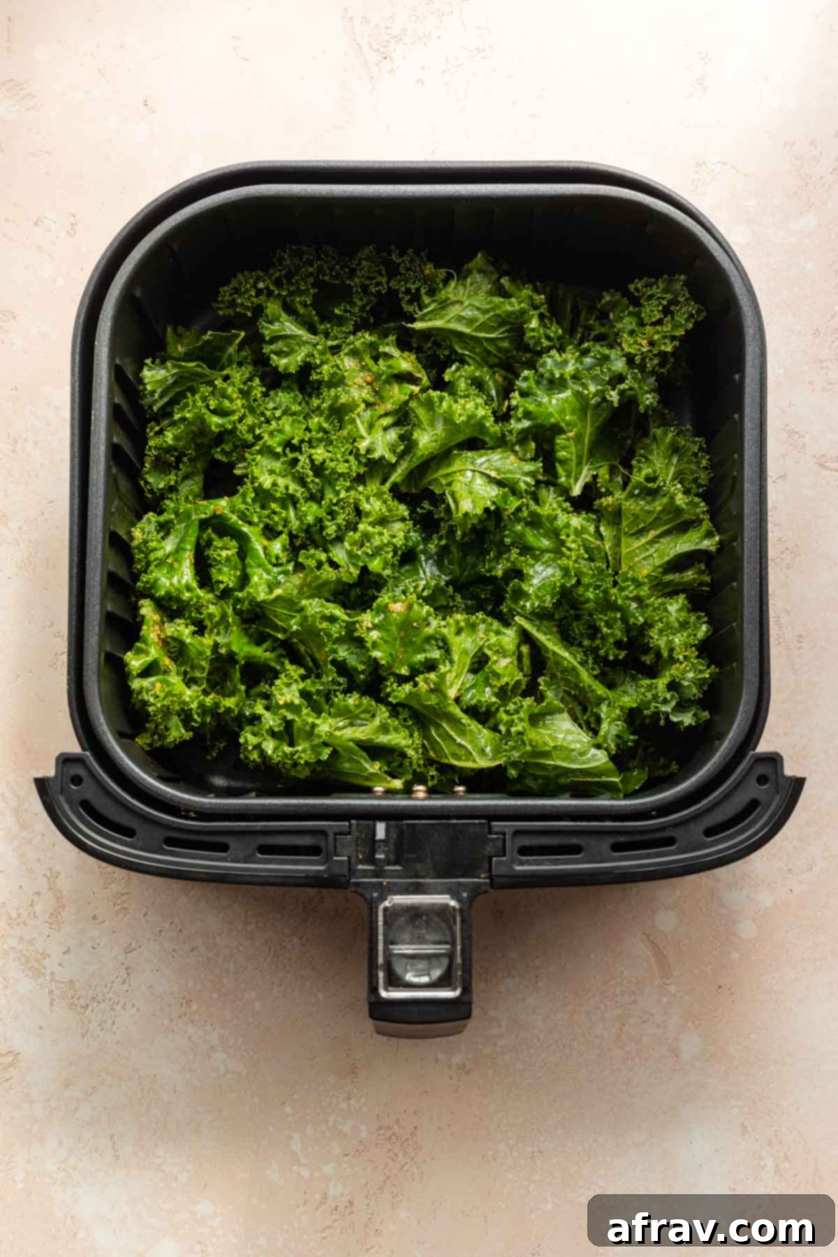 Overhead view of seasoned kale pieces evenly distributed in an air fryer basket, ready for the quick cooking process to transform them into crispy chips.