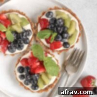 Effortless Fresh Vegan Fruit Tarts 12 Three mini fruit tarts on a small white plate with 2 vintage forks on the plate and fresh berries off to the side, highlighting the deliciousness.