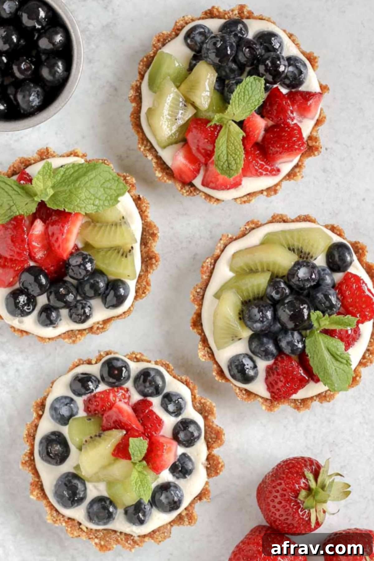 Effortless Fresh Vegan Fruit Tarts 4 Four beautifully arranged mini fruit tarts displayed on a sleek gray surface, showcasing their vibrant colors and appealing texture.