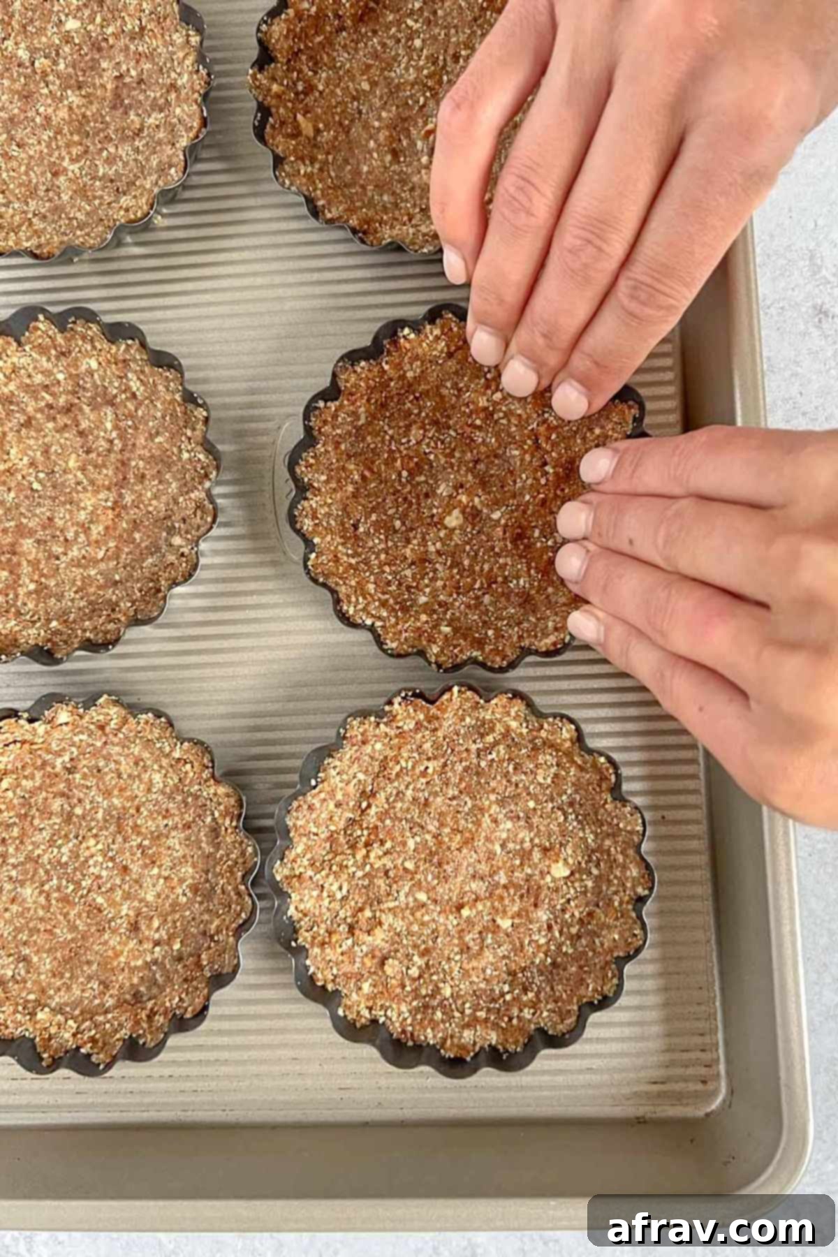 Effortless Fresh Vegan Fruit Tarts 7 A pair of hands meticulously pressing the vegan fruit tart crust into mini tart molds, shaping the edges with care.