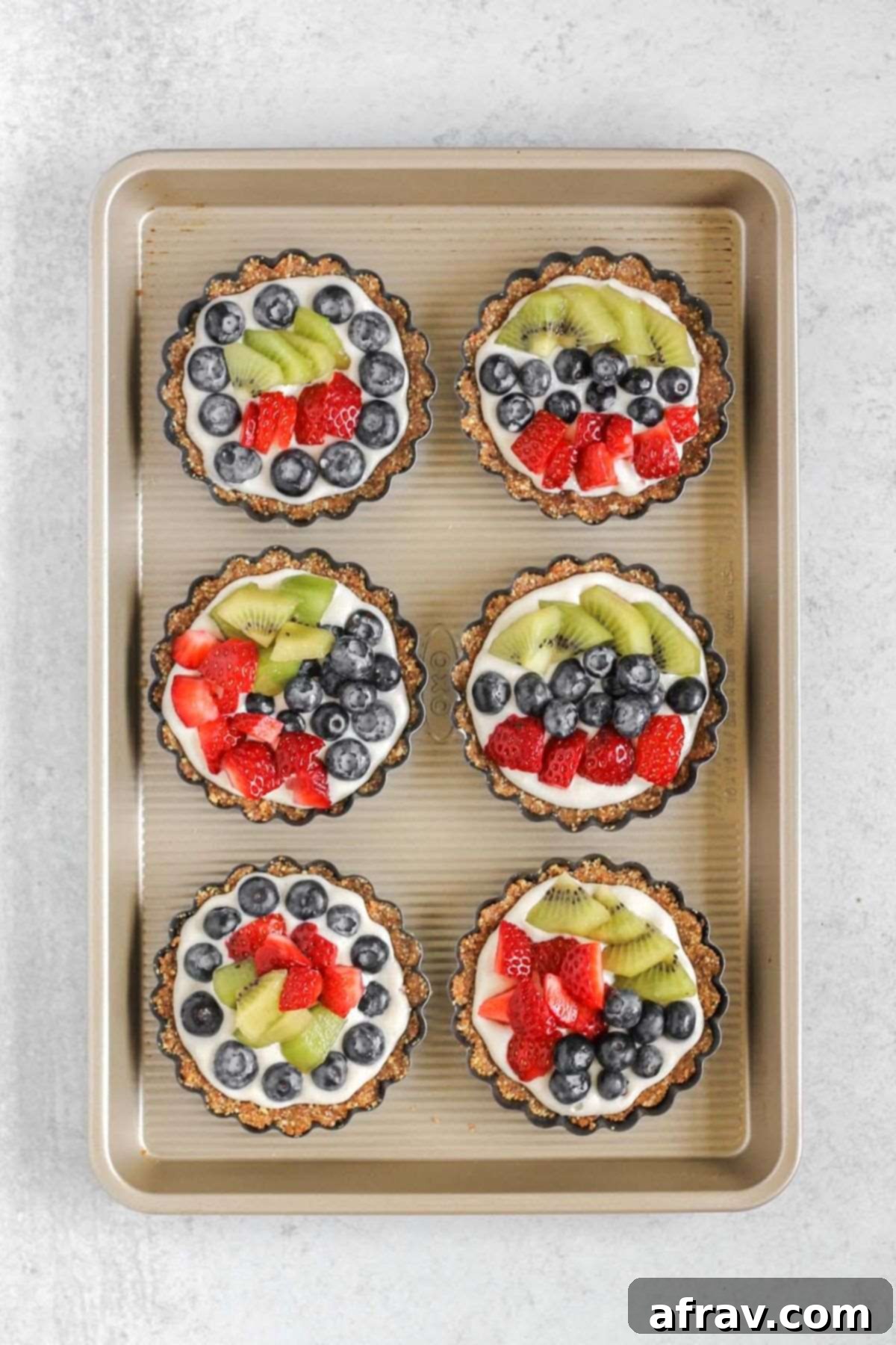 Effortless Fresh Vegan Fruit Tarts 10 A golden baking sheet holds several mini fruit tarts, now adorned with vibrant fresh fruit toppings, glistening and ready to chill.