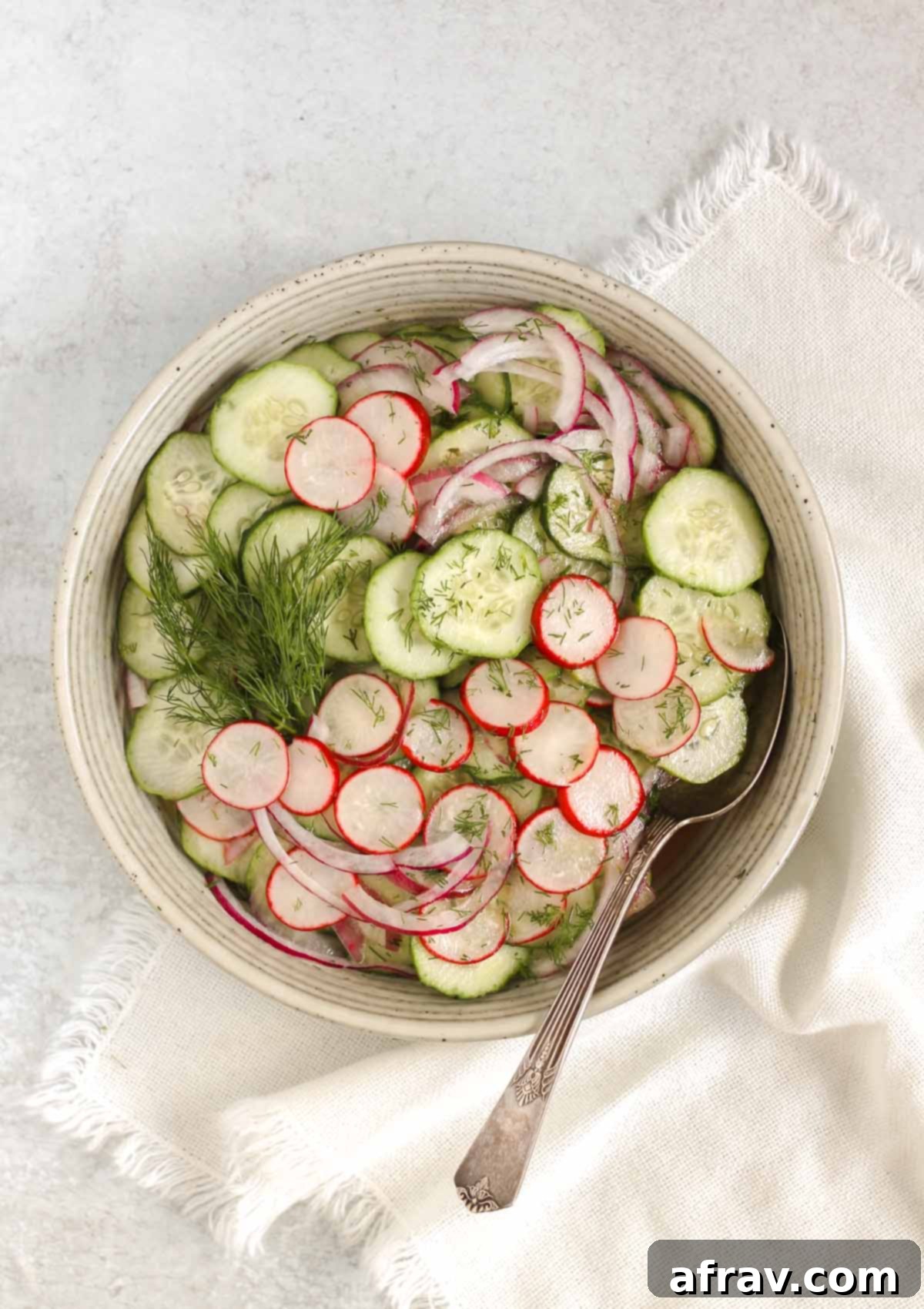 Cucumber radish salad in a serving bowl with red onion and a vintage serving spoon, and sprigs of fresh dill.