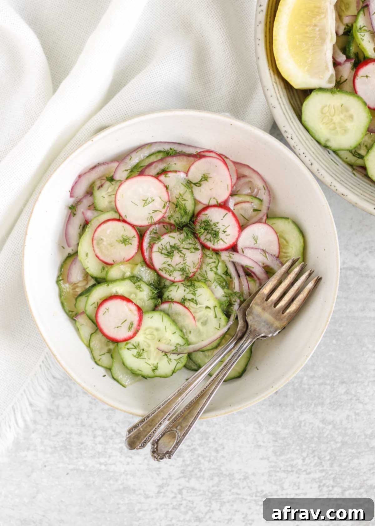 Cucumber radish salad on a small plate with two vintage forks and a bowl of the salad off to the side.