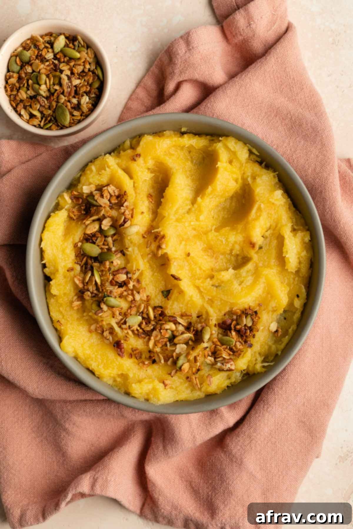 Acorn squash mash in a beige bowl and topped with savoury granola, ready to be served.