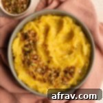 Mashed acorn squash in a bowl on a pink cloth with savoury granola on top.