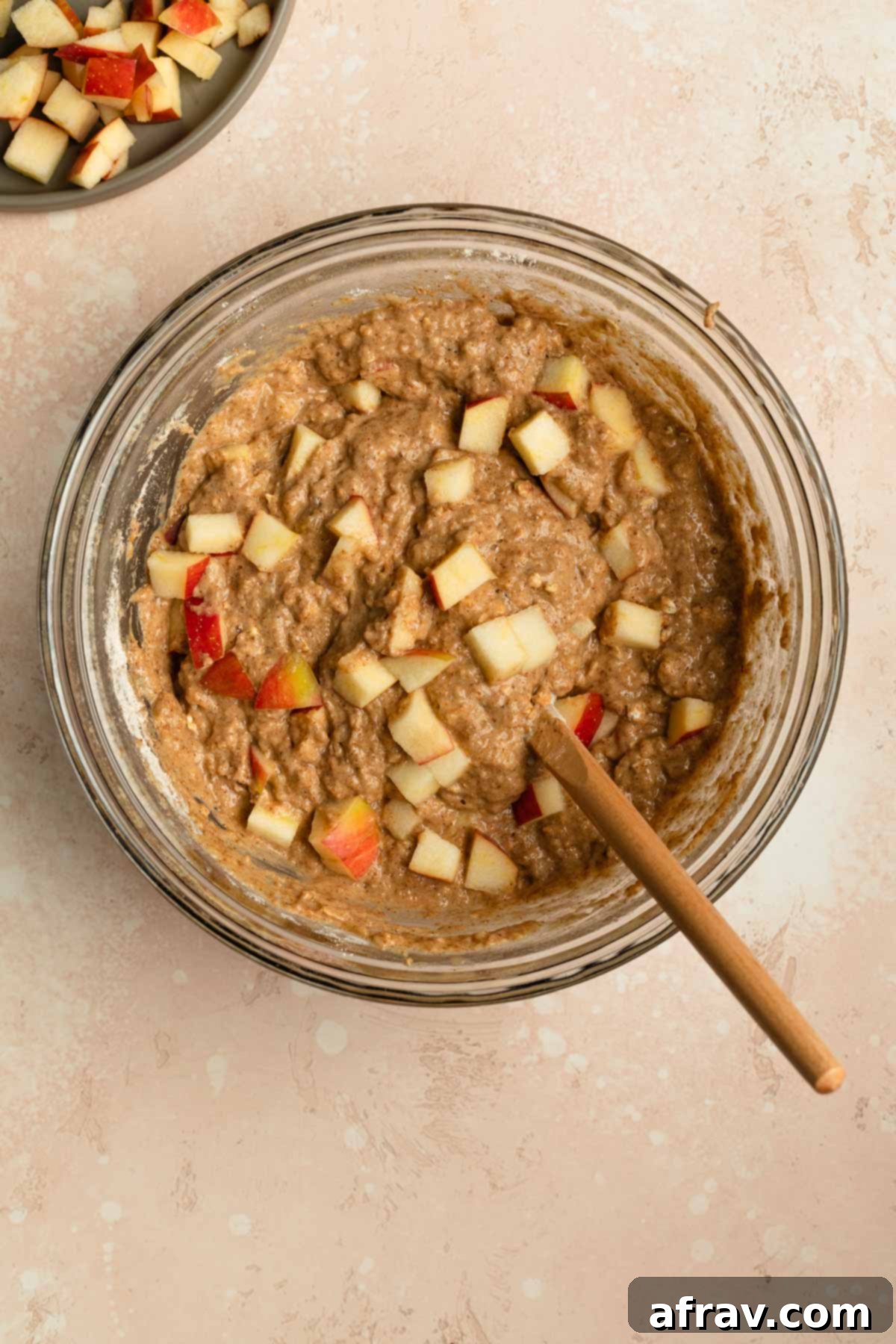 Muffin batter in a glass bowl with diced apple stirred into it, ready to be scooped.