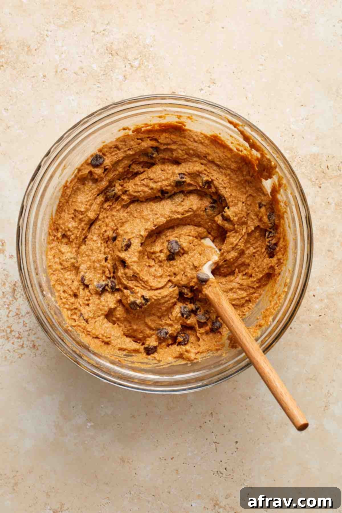 Muffin batter in a glass bowl with chocolate chips stirred in with a spatula.