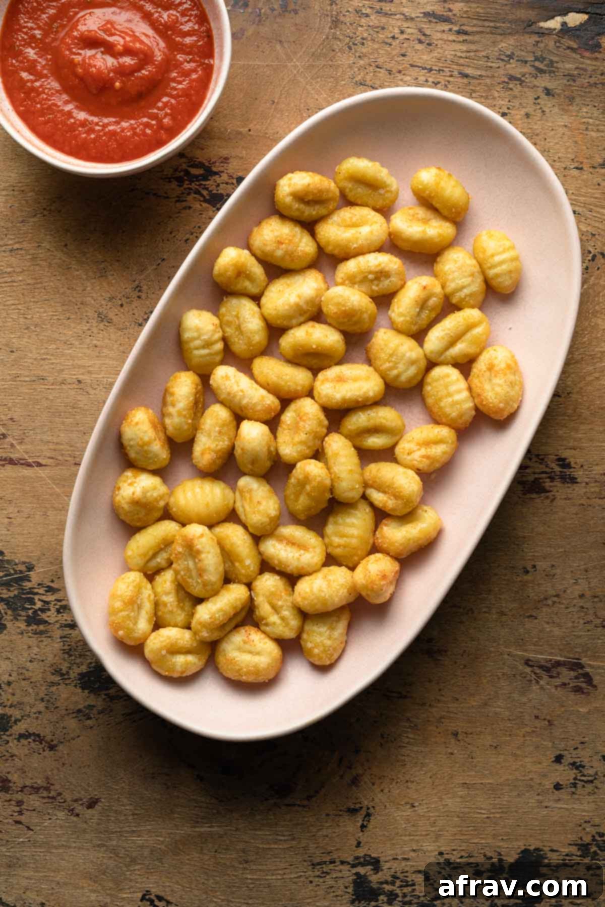 Crispy Air Fryer Gnocchi 2 Crispy gnocchi served on a pink platter next to a small bowl of marinara sauce, garnished with fresh basil.