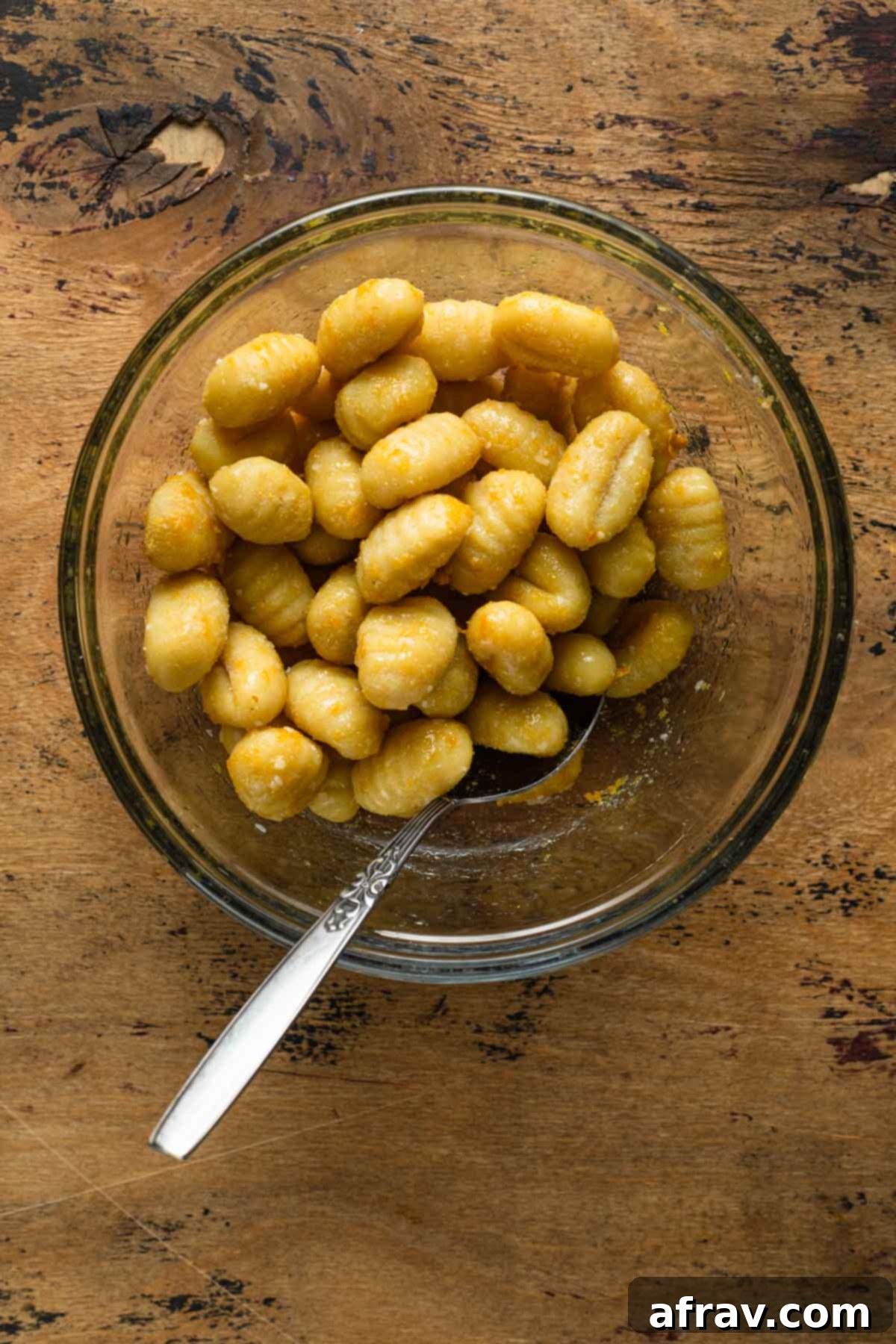 Seasoned gnocchi in a glass bowl with a spoon, ready for the air fryer.