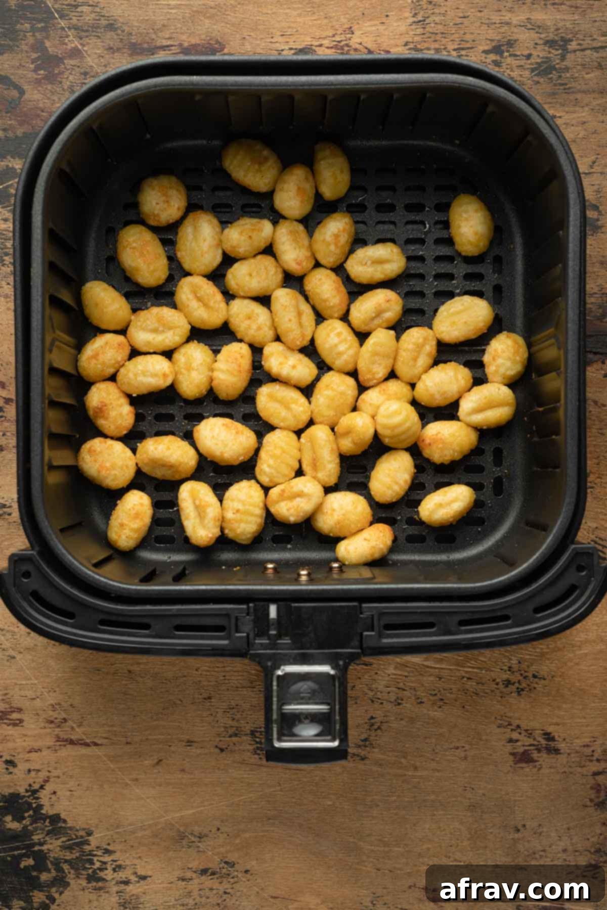 Air fried gnocchi piled in an air fryer basket after cooking, showcasing their crispy exterior.
