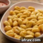 Crispy Air Fryer Gnocchi 7 Close up view of air fryer gnocchi in a serving dish next to a bowl of marinara sauce, perfect for a quick meal.
