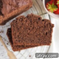Two slices stacked of chocolate protein banana bread on a round wire cooling rack with a bowl of strawberries to the side.