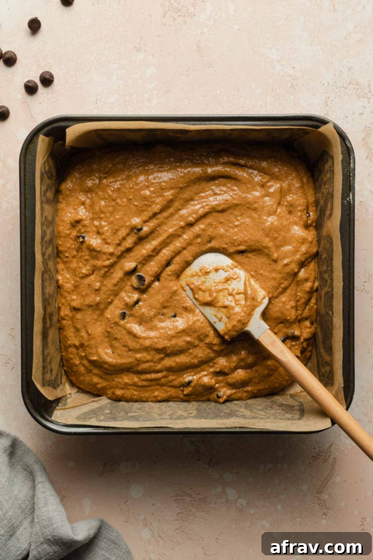 Pumpkin cake batter spread out evenly in a square baking pan with a spatula, ready to be baked.