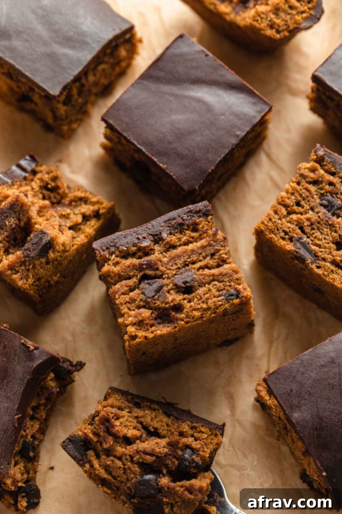 Pieces of pumpkin cake, generously topped with dairy-free chocolate ganache and arranged on parchment paper, ready to be enjoyed.
