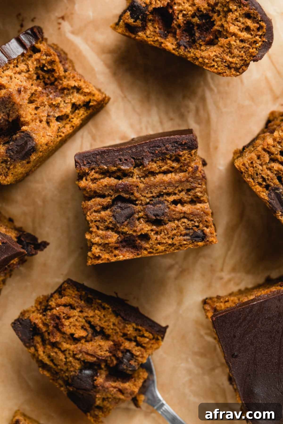 Close up view of a perfectly cut piece of pumpkin snack cake, showing its moist interior, dark chocolate chips, and thick chocolate ganache topping.