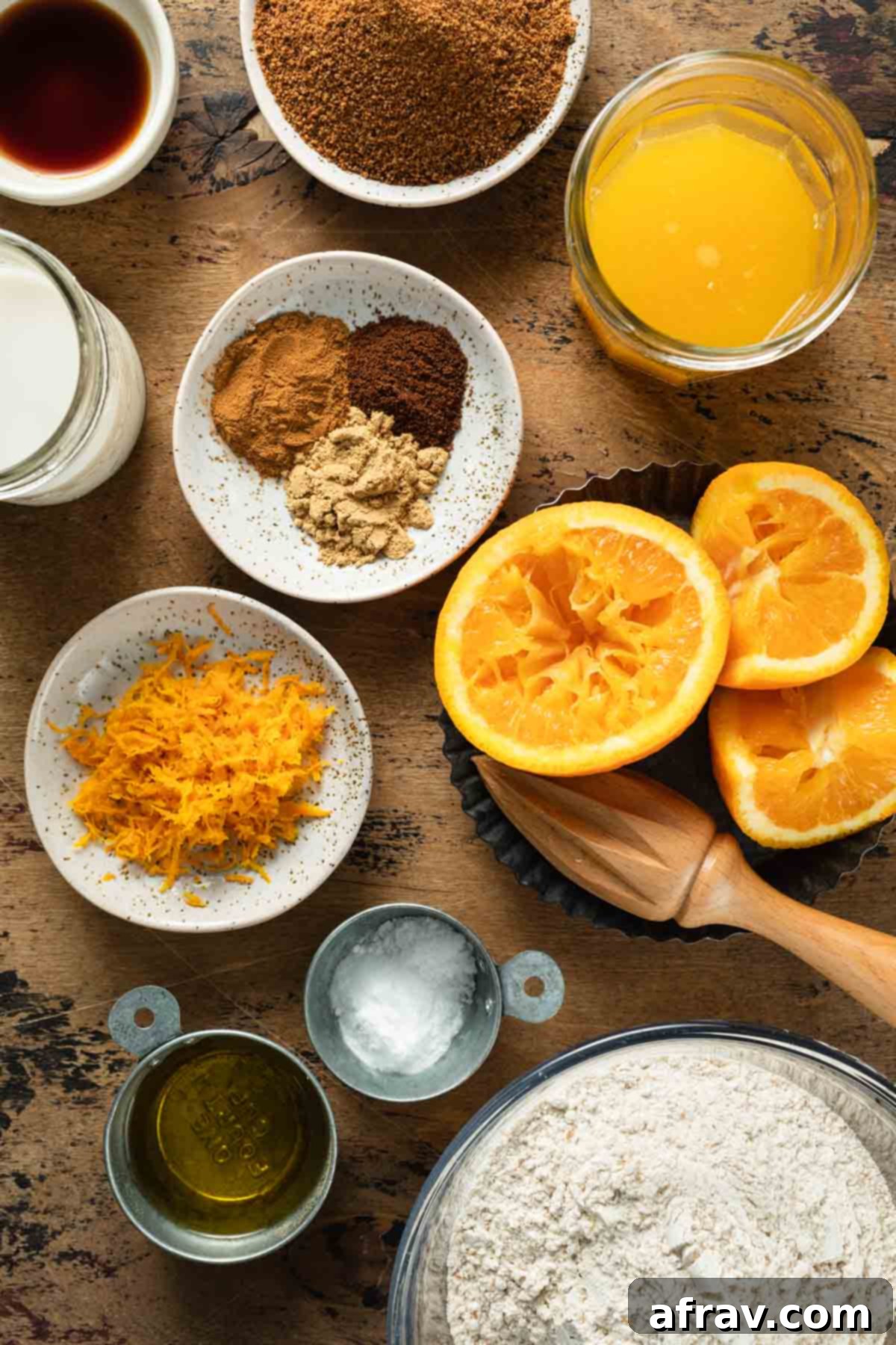 Various essential ingredients for baking orange spice cake, including whole oranges, ground spices, flour, and milk, neatly arranged on a countertop.