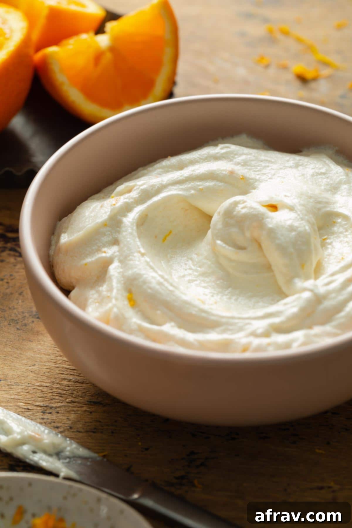 Side view of fluffy orange cream cheese frosting in a pink mixing bowl, showing its light and airy texture.