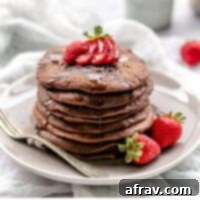 Chocolate pancakes topped with strawberries and dripping with syrup on a plate with a vintage fork.