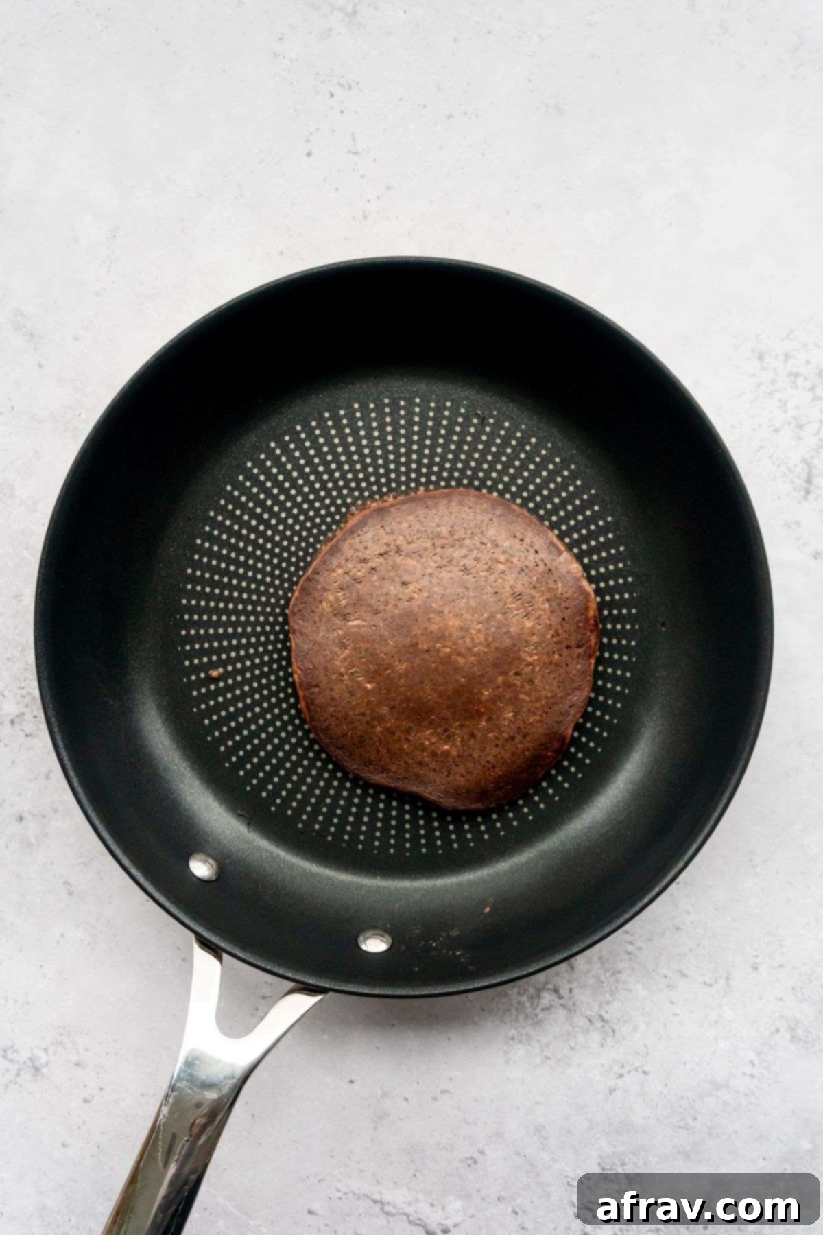 A perfectly golden brown chocolate pancake cooking in a frying pan.