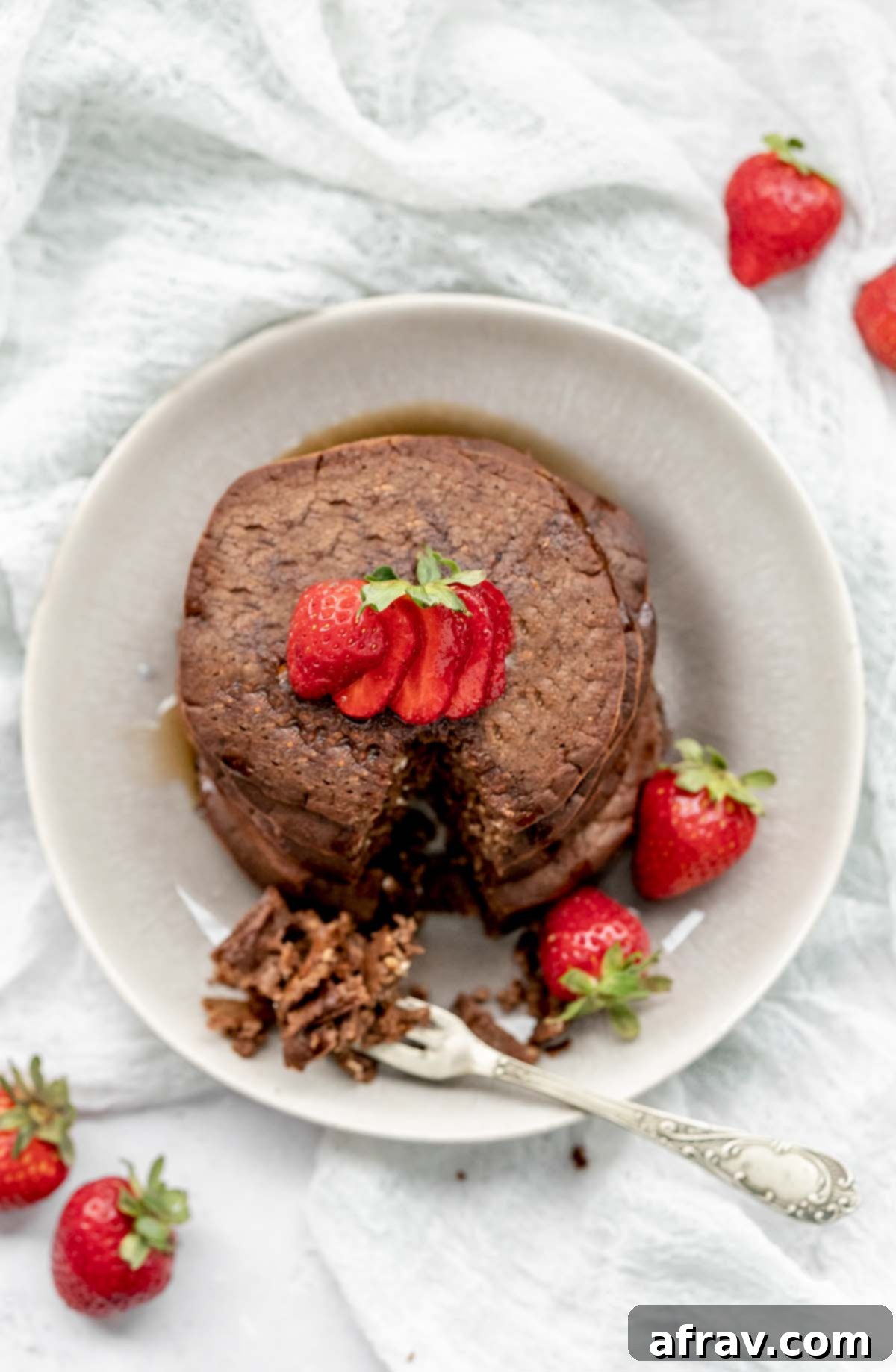 Overhead view of chocolate protein pancakes and strawberries on a plate with a small triangle cut from the pancakes.
