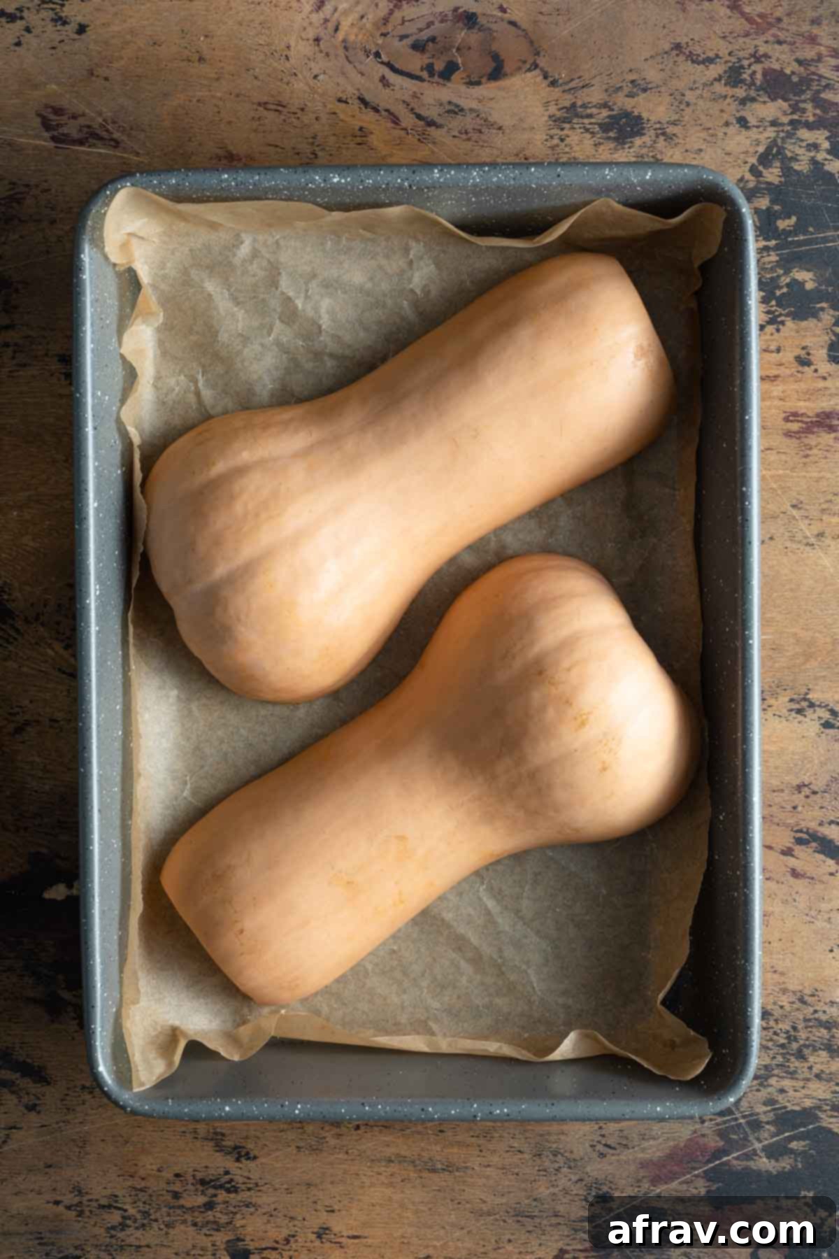 Two squash halves resting cut side down in a roasting pan, ready for the oven.