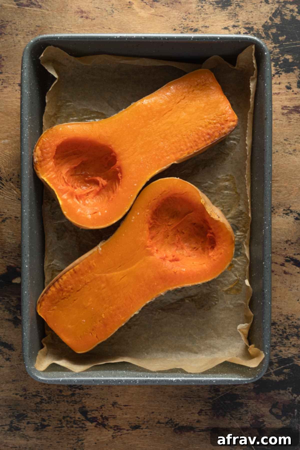 Overhead view of two roasted squash halves in a pan, their flesh softened and lightly caramelized.