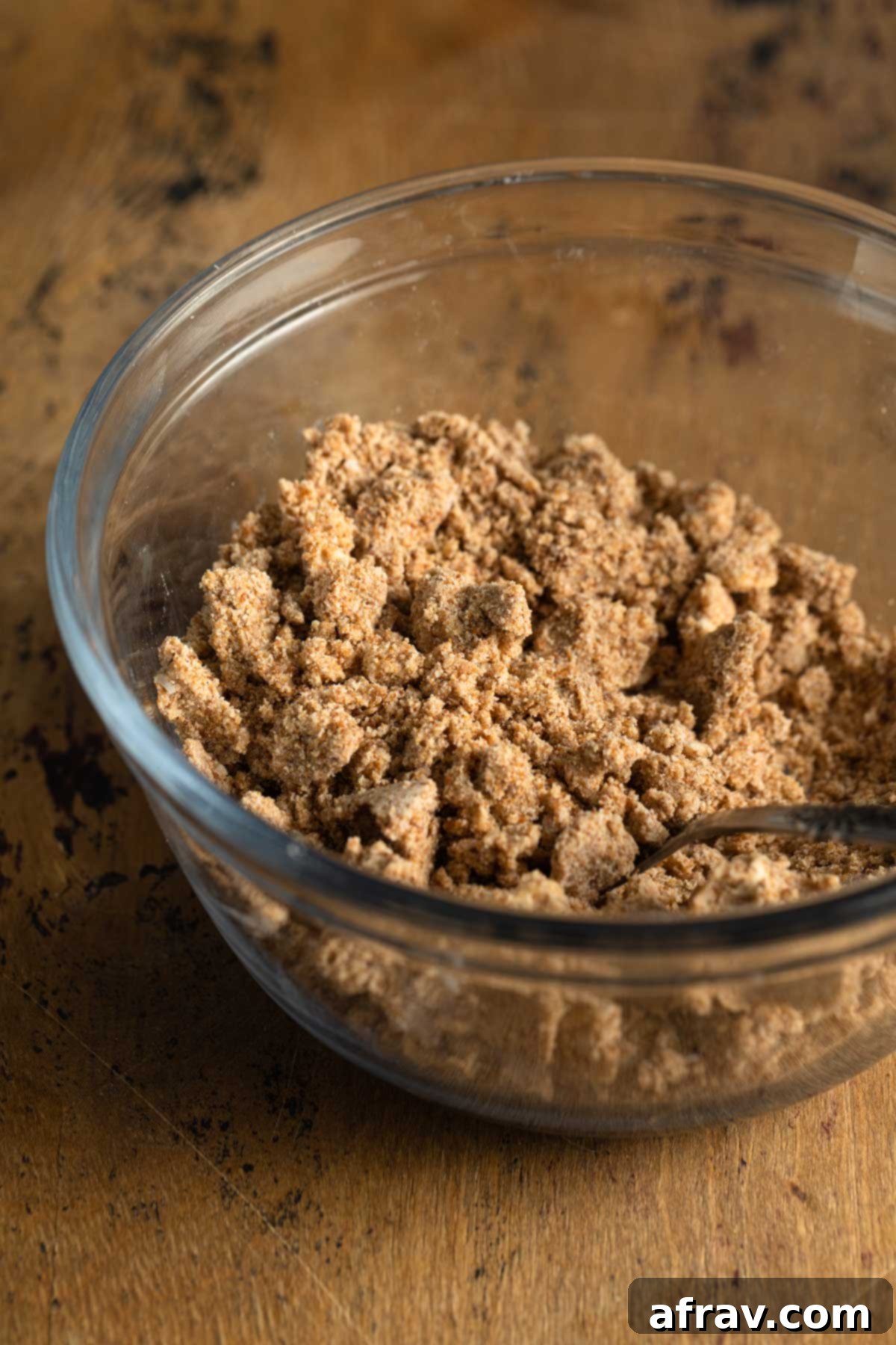 Side view of crumb topping mixture in a clear glass bowl, showing the distinct buttery crumbs.
