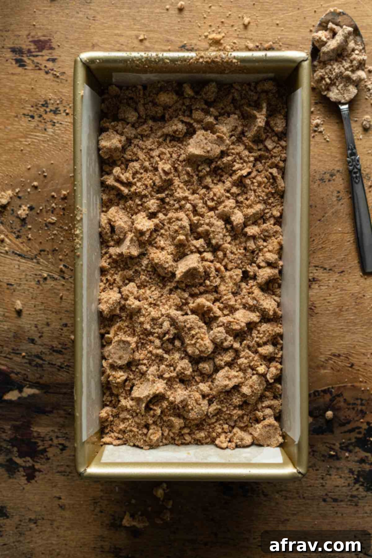 Bread batter in a loaf pan, evenly topped with the buttery crumb topping, ready for baking.