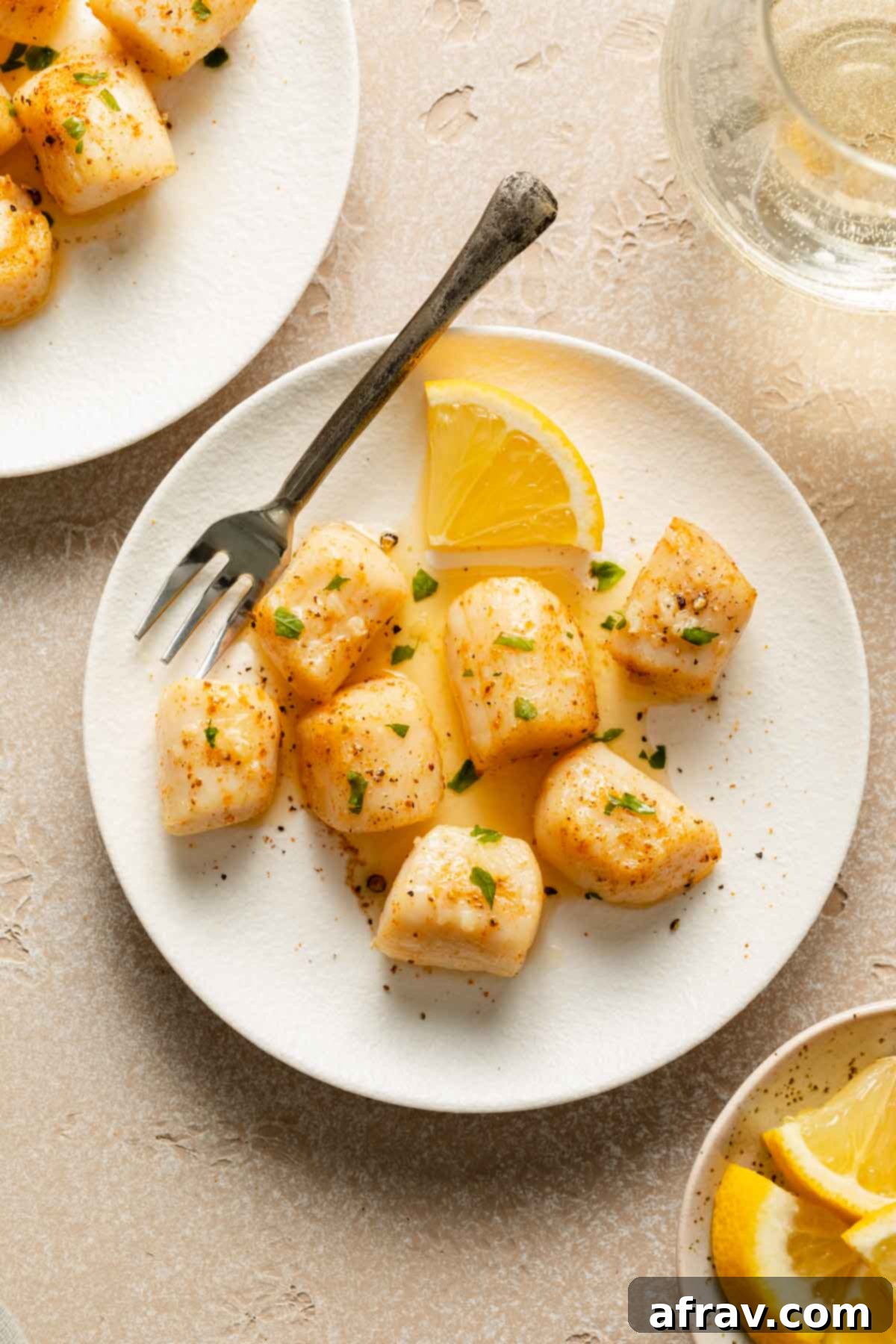 Air Fryer Scallops 2 Scallops topped with melted butter and chopped parsley on a white plate.