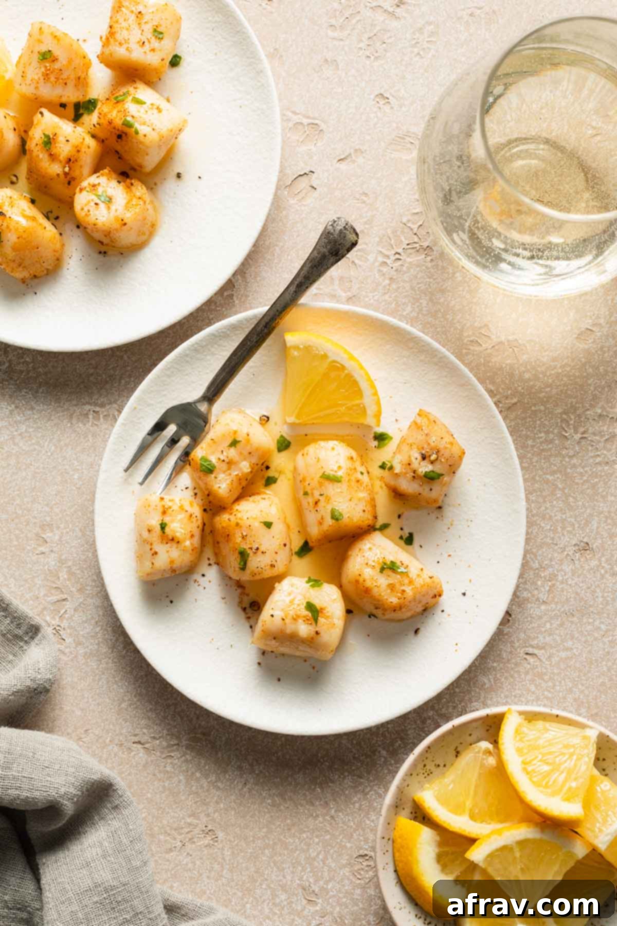 Air Fryer Scallops 7 Air fried scallops arranged on two white plates next to lemon wedges and a glass of wine.
