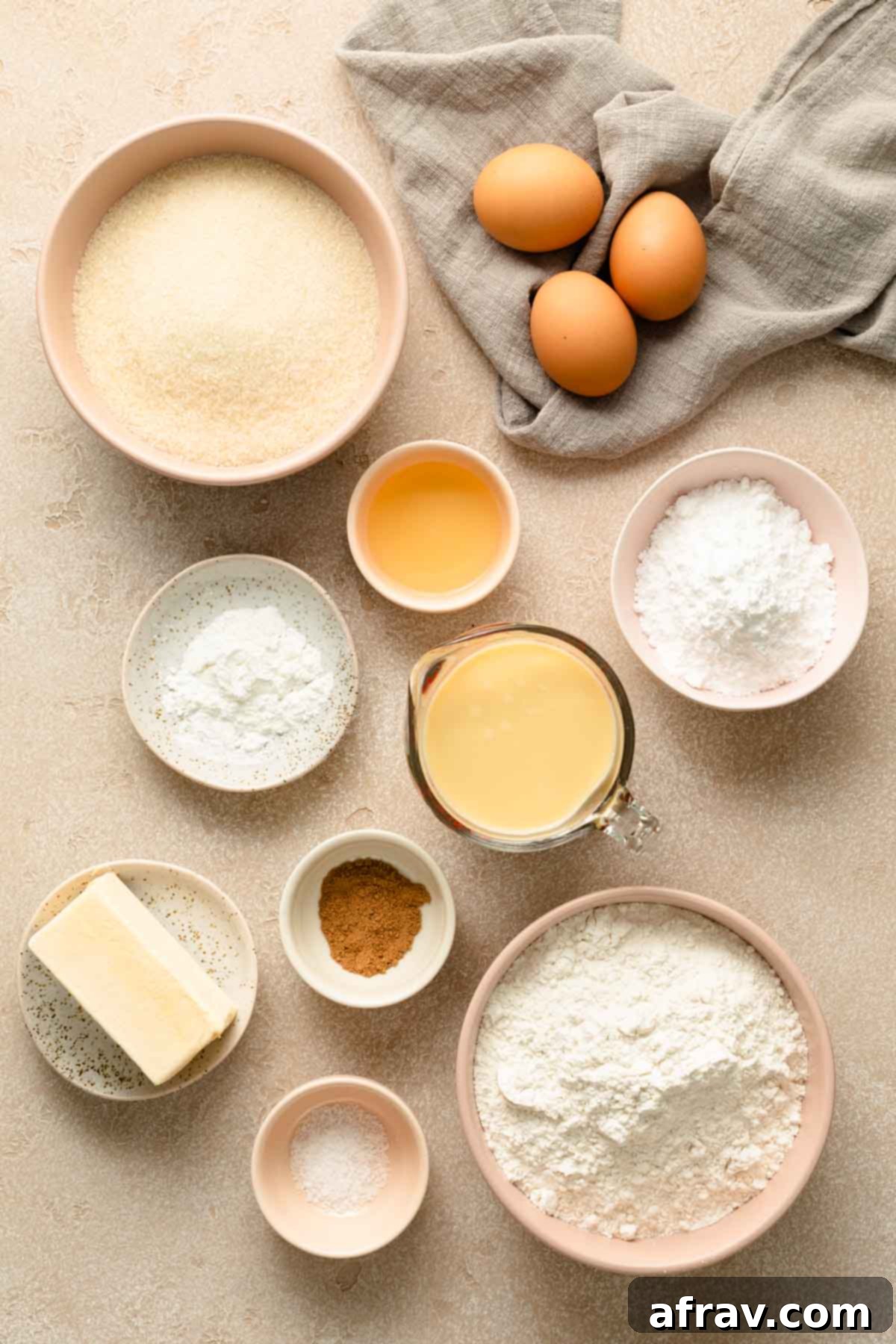 Arrangement of all ingredients needed for Eggnog Bundt Cake: flour, sugar, butter, eggs, eggnog, rum, nutmeg, baking powder, salt, and powdered sugar for the glaze, neatly organized on a wooden surface.