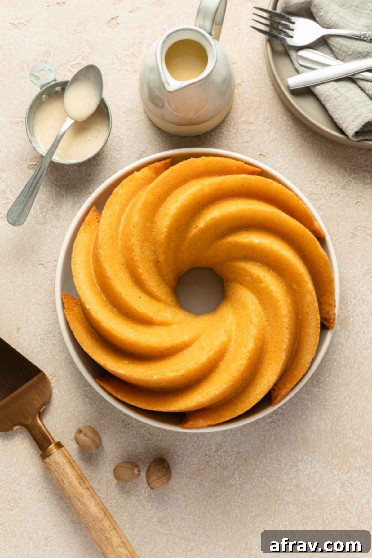 A beautifully baked golden-brown Eggnog Bundt Cake resting on a round plate, unglazed and cooling on a wire rack, showcasing its perfect shape and crispy edges.