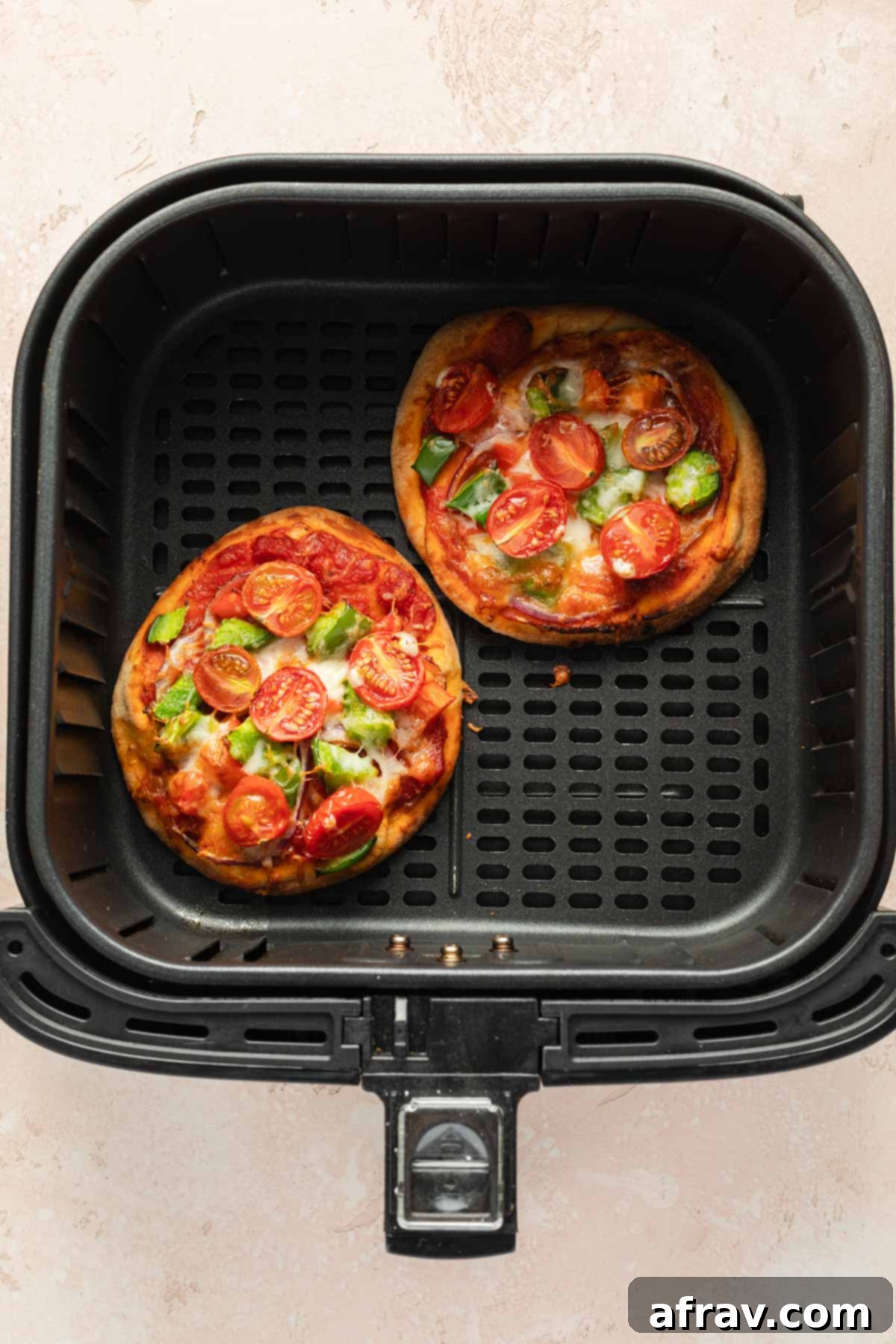 Two mini pizzas in an air fryer basket.