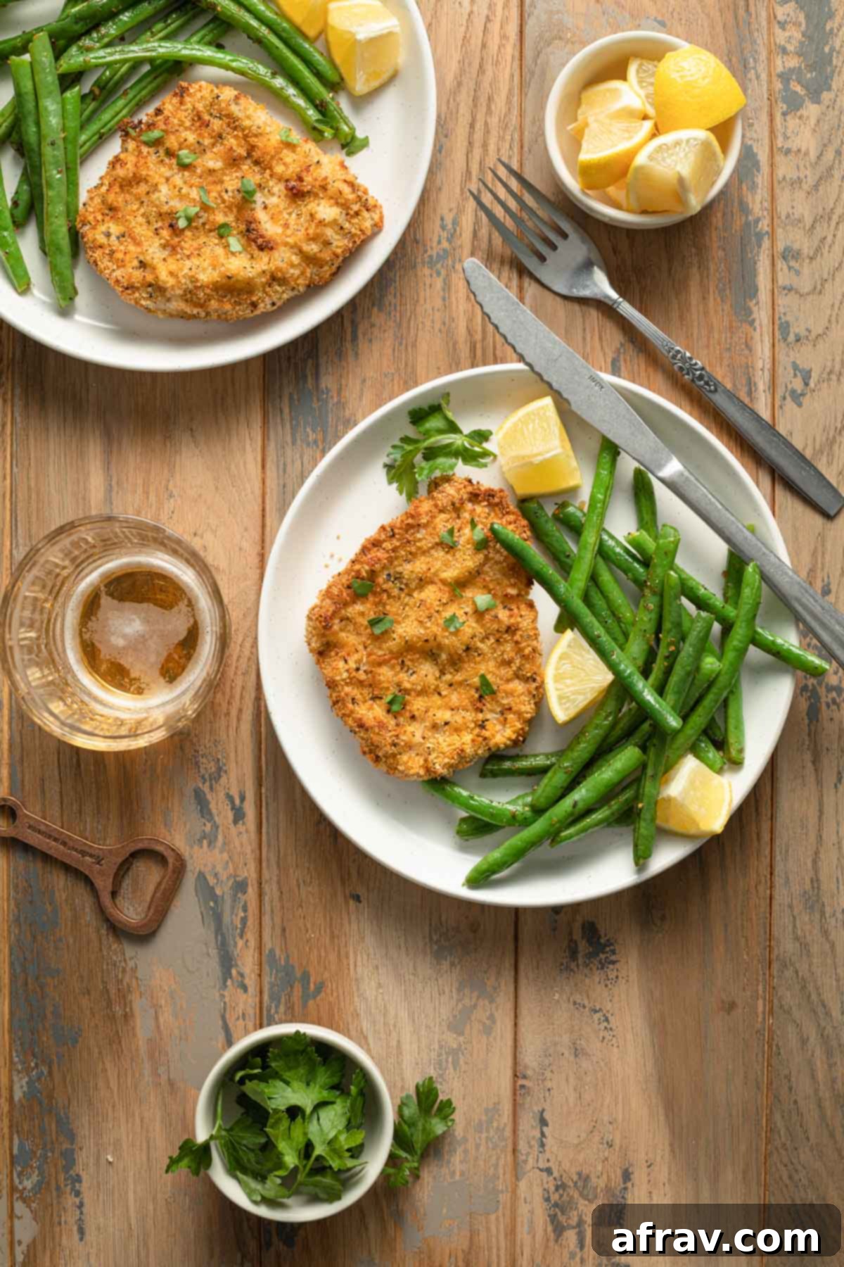 Crispy Air Fryer Pork Schnitzel 2 Two plates of crispy Air Fryer Pork Schnitzel, served with vibrant green beans and fresh lemon wedges, ready to be enjoyed.