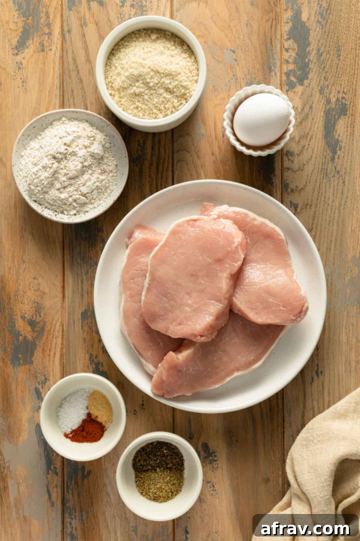 Crispy Air Fryer Pork Schnitzel 3 A beautiful arrangement of fresh ingredients for Air Fryer Pork Schnitzel, including pork chops, flour, eggs, panko crumbs, and various seasonings, all individually placed and ready for preparation.