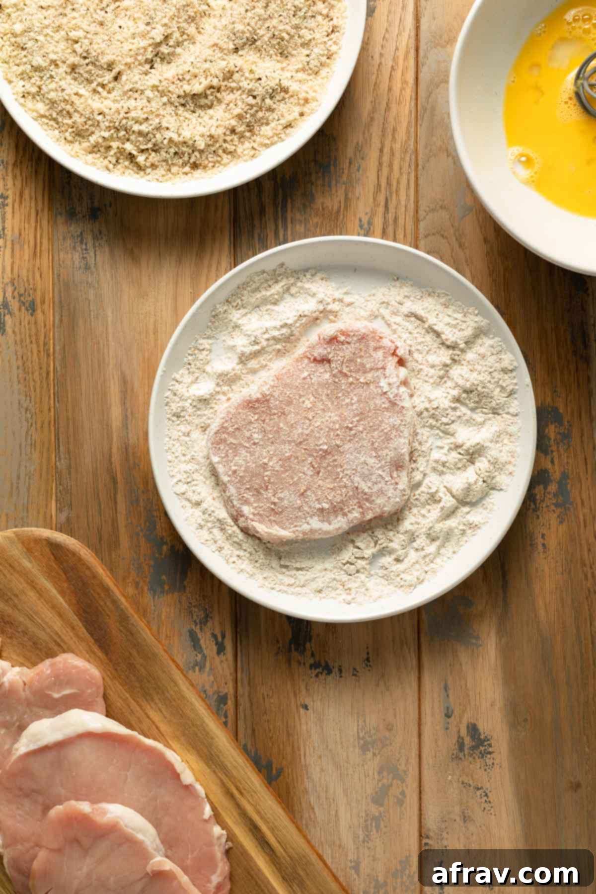 A thin pork cutlet lightly coated in flour, resting on a plate, ready for the next breading step.
