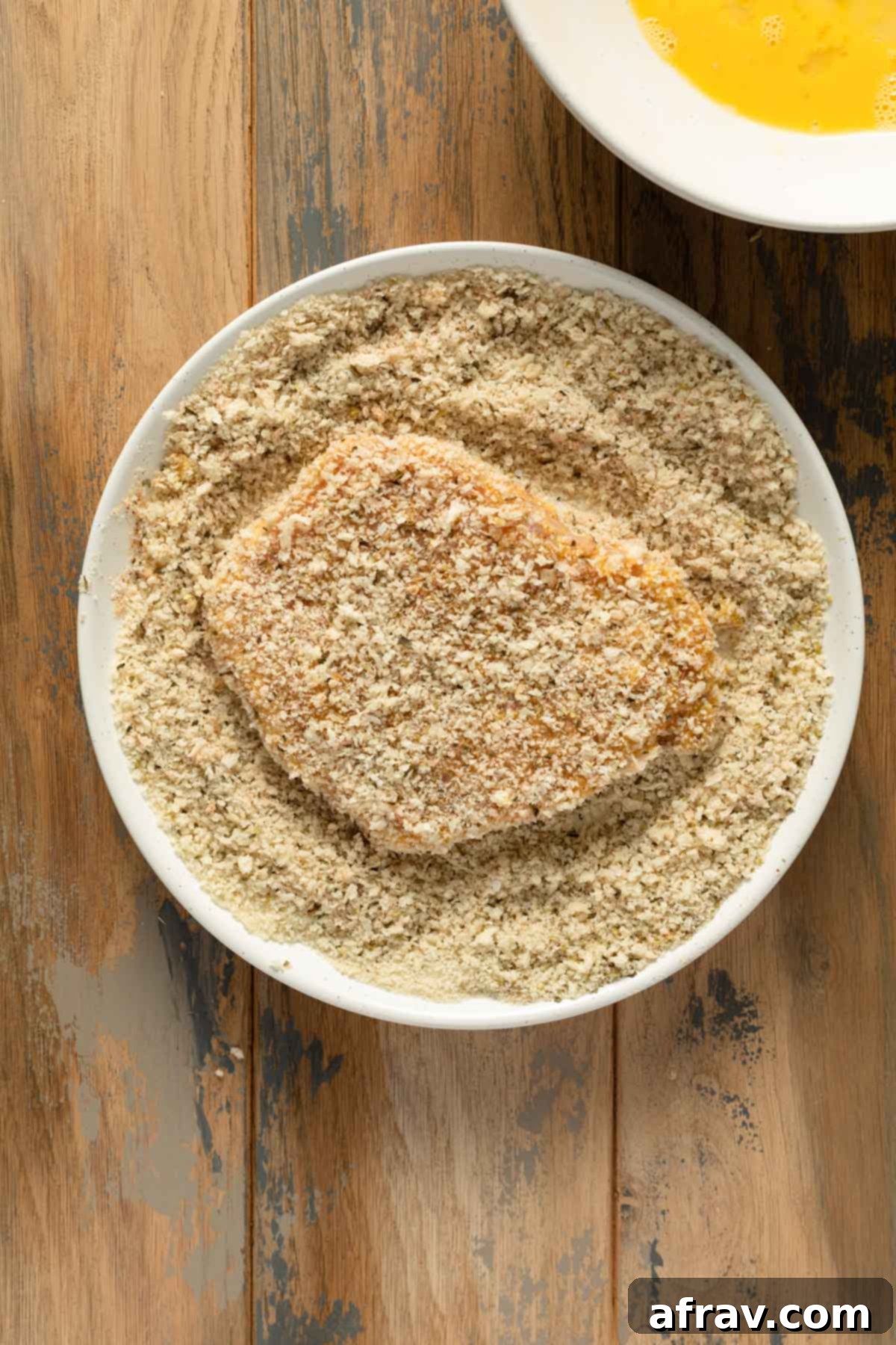 A fully breaded pork cutlet, covered in crispy panko crumbs, on a plate, perfectly prepped for air frying.